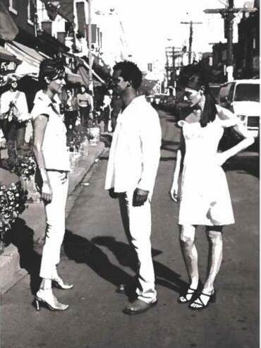 Three stylish individuals converse on a city street, dressed in monochrome, fashionable attire.